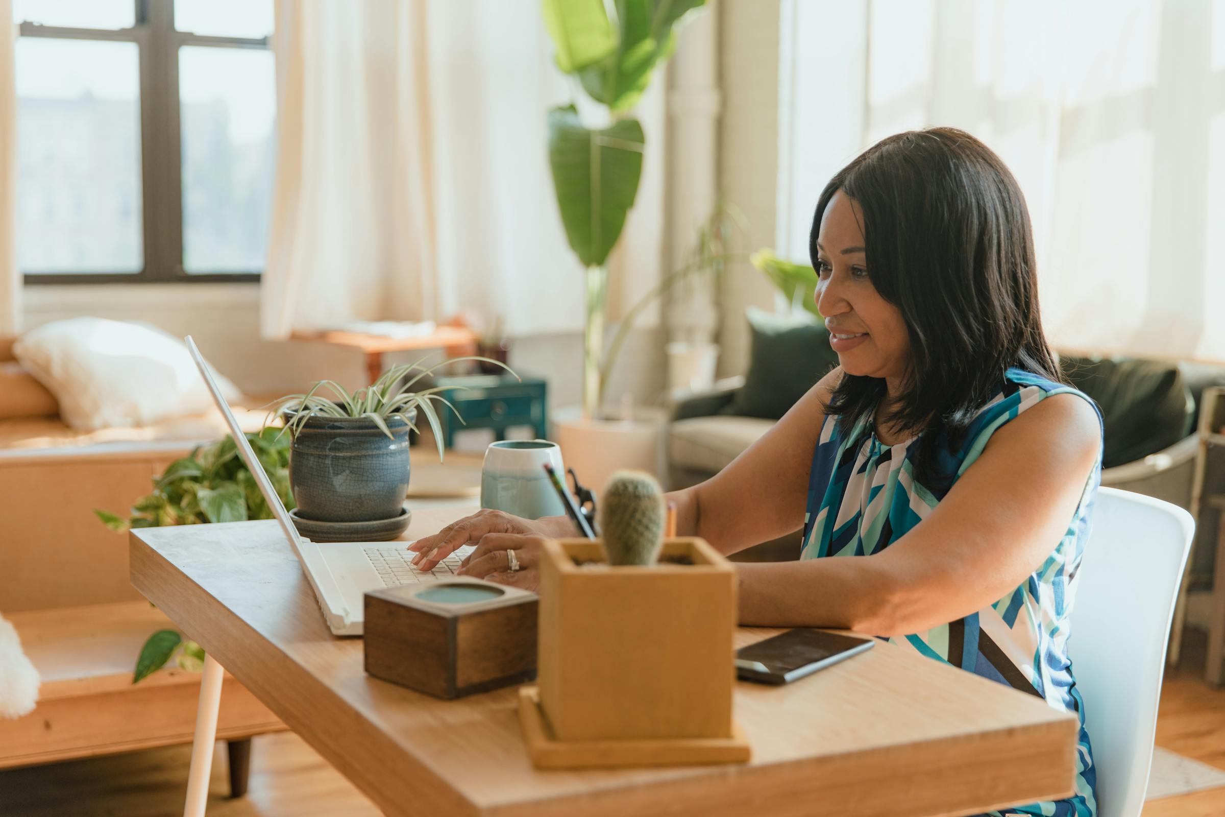 Person using a laptop in a warm home setting with plants and a comfortable workspace